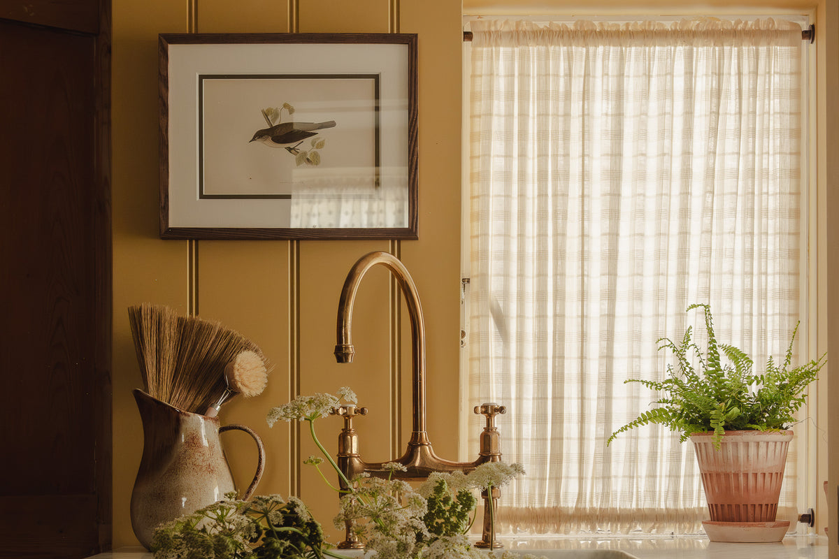 Double rod pocket café curtain in Elva cotton check, on brass poles top and bottom in a utility room at Baywell Studio