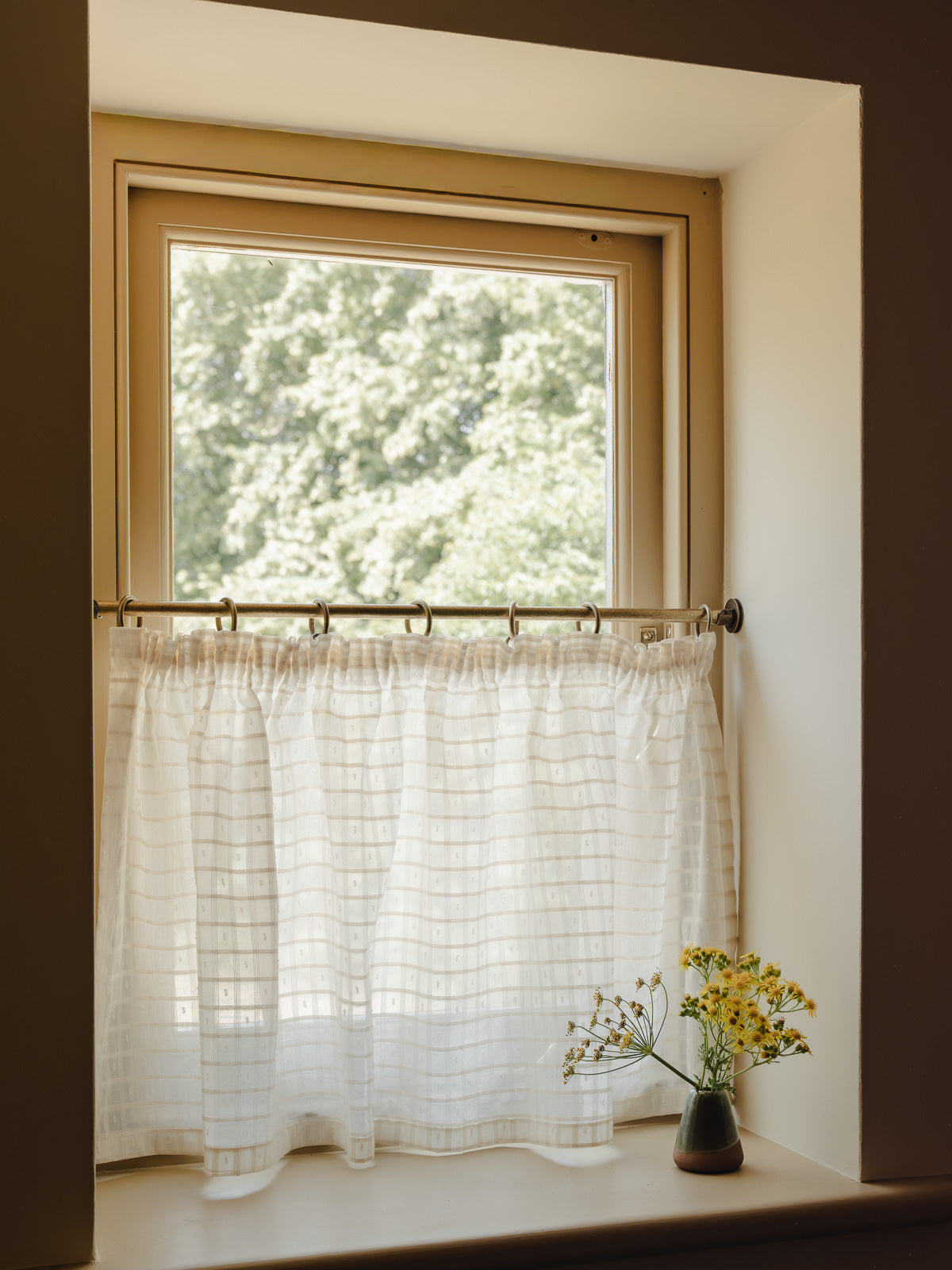 Pleated café curtain in sheer Alda cotton on brass rings and pole in a bright hallway 