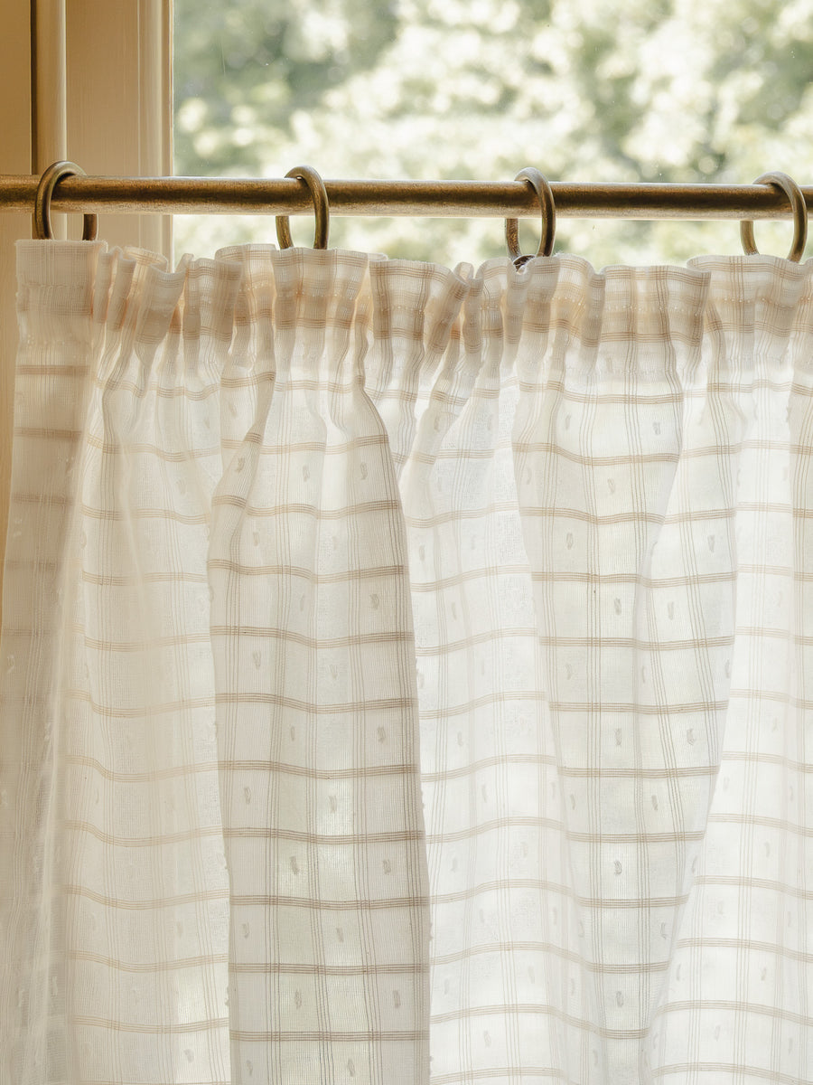 Close-up pleated café curtain in sheer Alda cotton on brass rings and pole in a bright hallway 