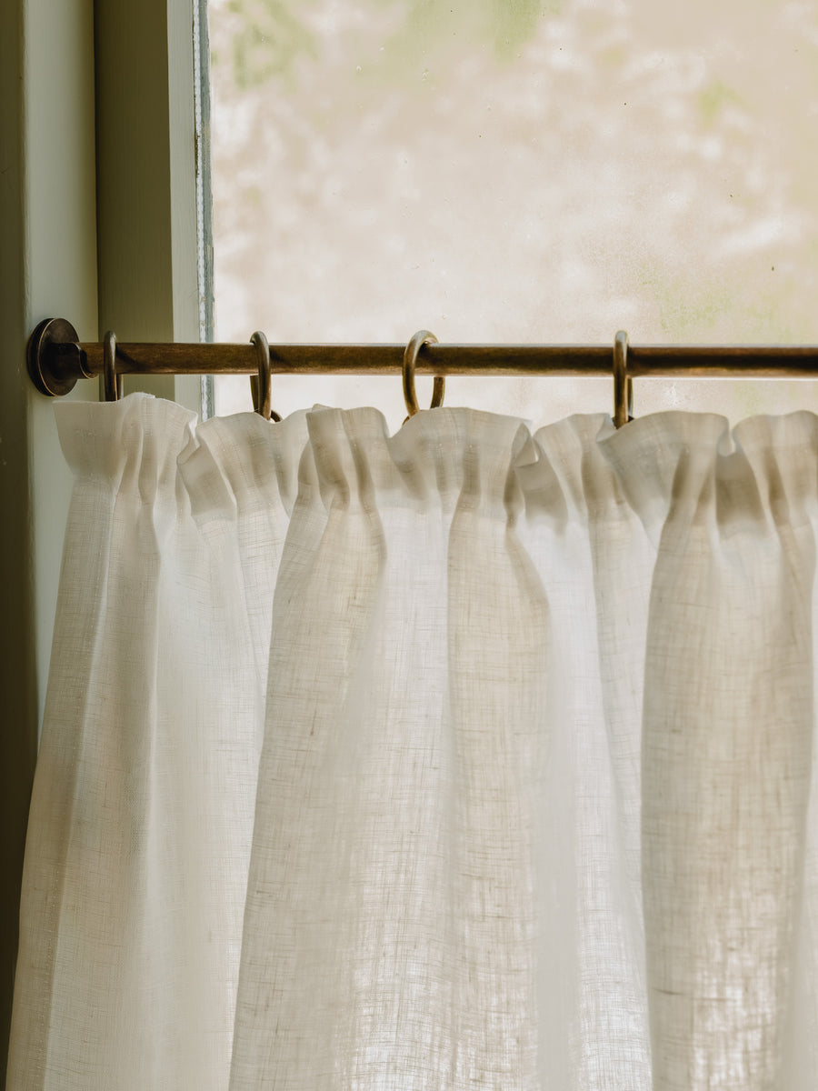 Close-up pleated café curtain in white Luma linen on brass rings and pole, in a bathroom at Baywell Studio