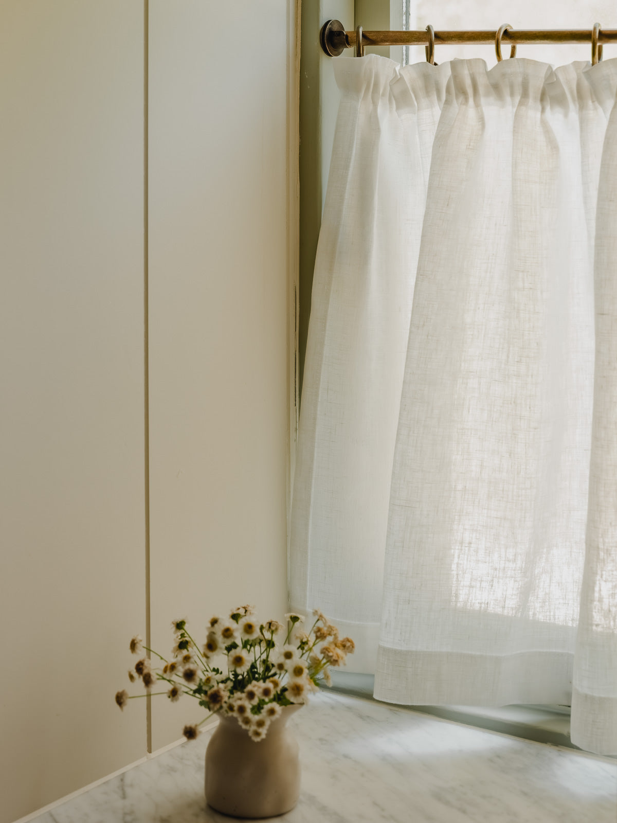 Close-up pleated café curtain in white Luma linen on brass rings and pole, in a bathroom at Baywell Studio