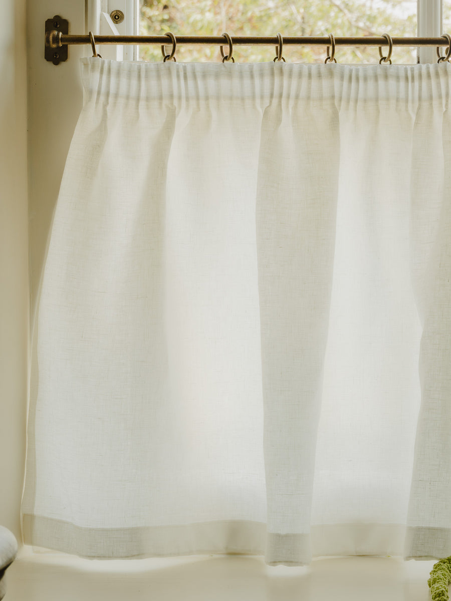Close-up pleated café curtain in white Luma linen on brass rings and pole, in a bright hallway at Baywell Studio