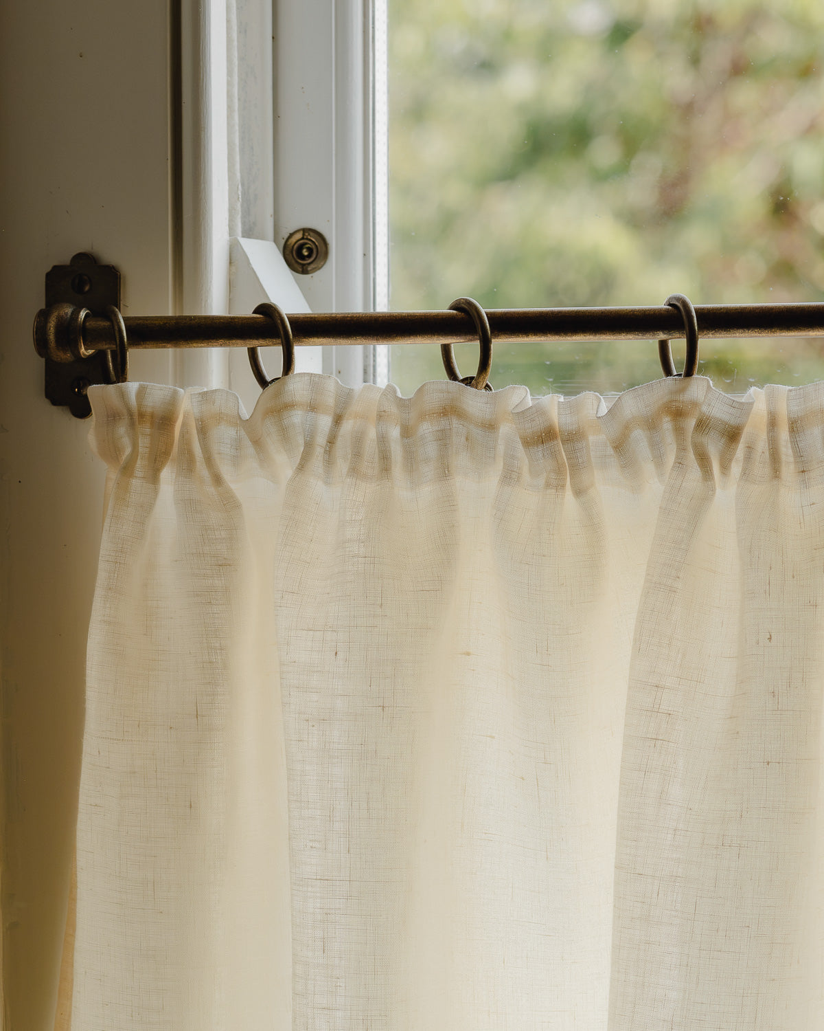 Close-up pleated café curtain in cream Sera linen on brass rings and pole, in a bright hallway at Baywell Studio