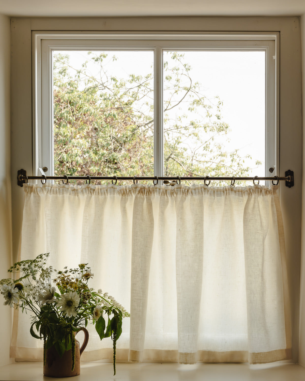 Close-up pleated café curtain in cream Sera linen on brass rings and pole, in a bright hallway at Baywell Studio