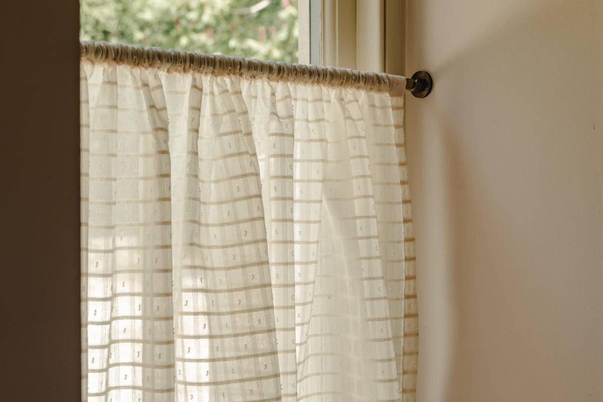 Close-up rod pocket café curtain in Alda, an Indian cotton fine weave, gathered on a slim brass pole in the cottage kitchen at Baywell Studio
