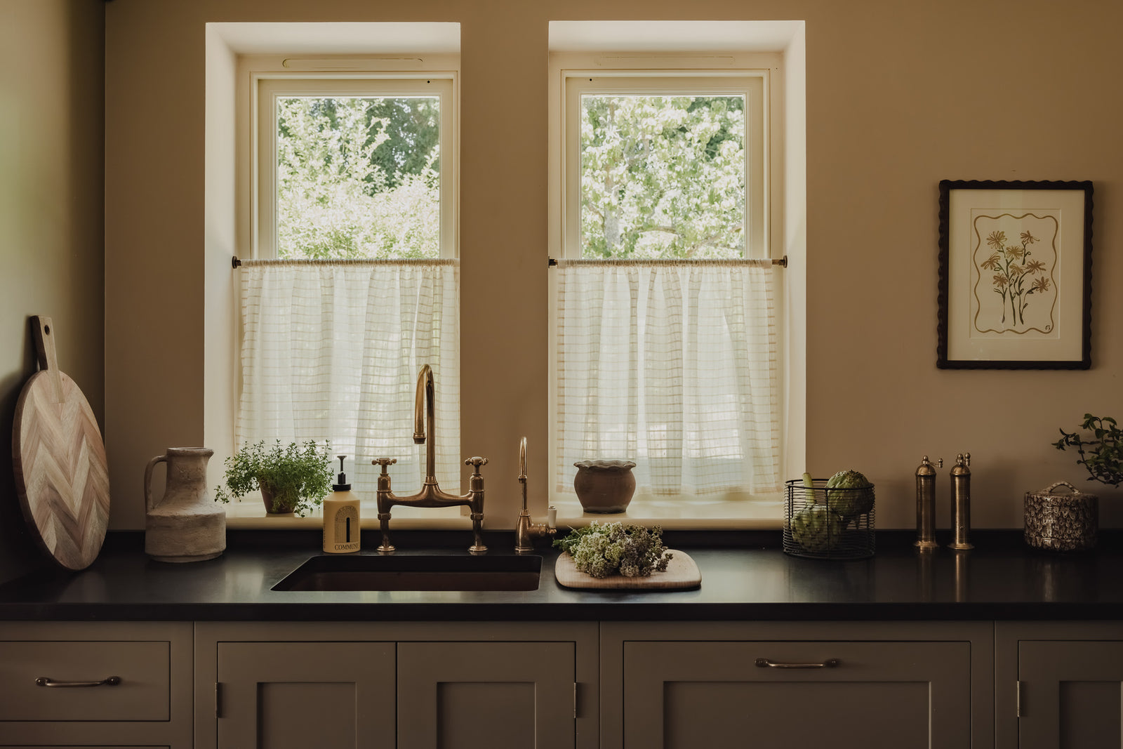 Rod pocket café curtains in Alda Indian cotton on slim brass poles, above a copper sink in the cottage kitchen at Baywell Studio
