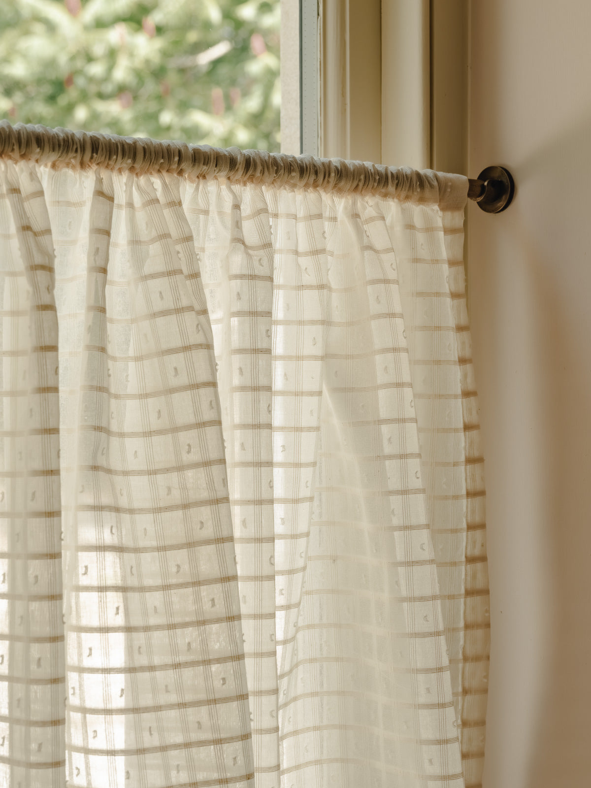 Close-up rod pocket café curtain in Alda, an Indian cotton fine check weave, gathered on a slim brass pole at Baywell Studio