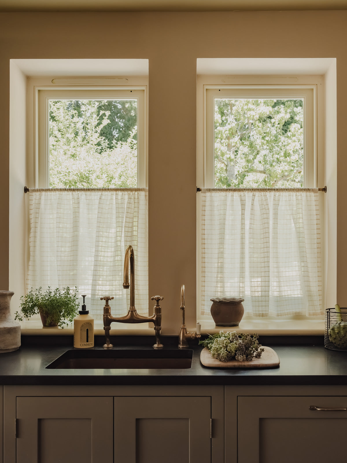 Rod pocket café curtains in Alda Indian cotton on slim brass poles, above a copper sink in the cottage kitchen at Baywell Studio