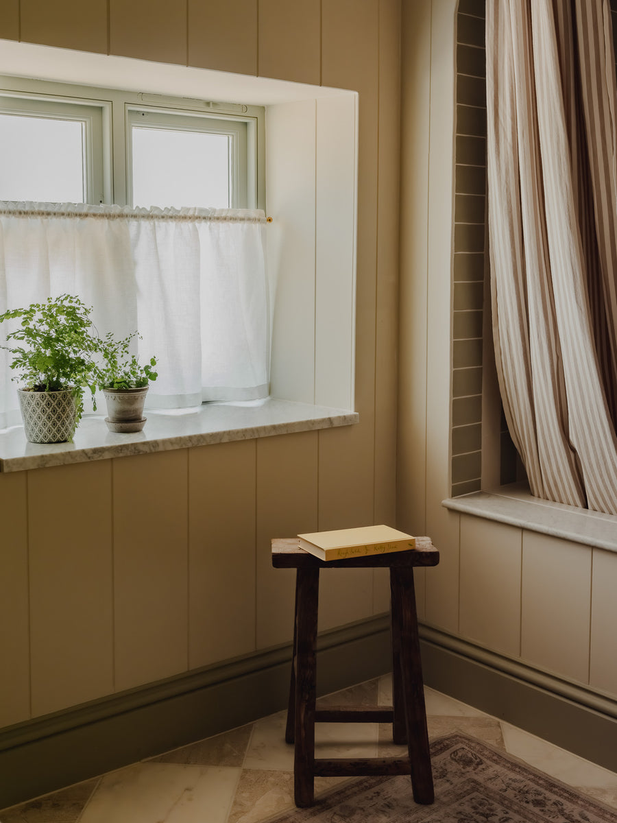 Ruffle-top rod pocket café curtain in cream Luma linen on a brass pole, in a family bathroom with ferns on the sill at Baywell Studio