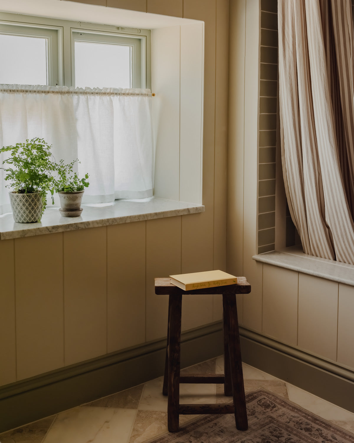 Ruffle-top rod pocket café curtain in cream Luma linen on a brass pole, in a family bathroom with ferns on the sill at Baywell Studio