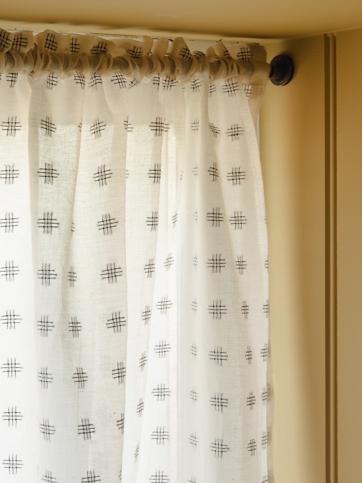 Rod pocket café curtain in Noma cotton with a woven check motif, on a slim brass pole in a cloakroom at Baywell Studio