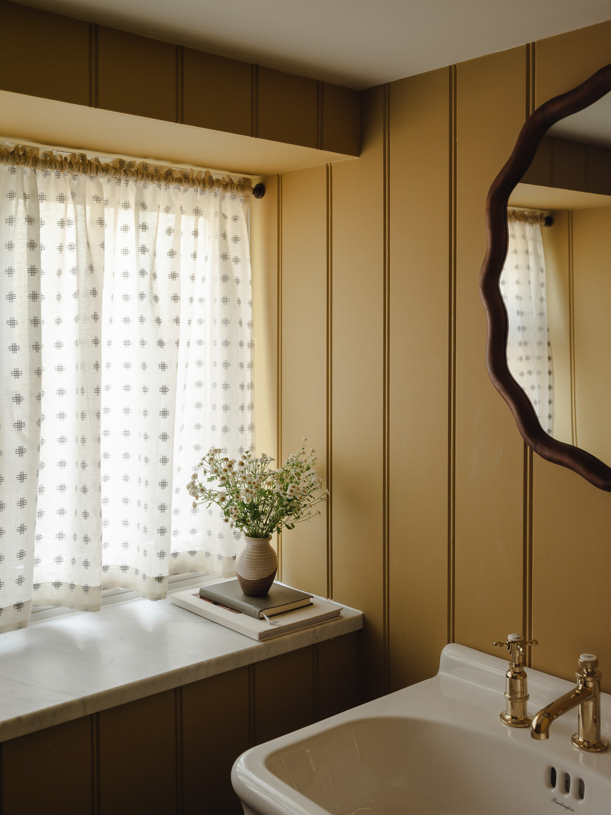 Rod pocket café curtain in Noma cotton with a woven check motif, on a slim brass pole in a cloakroom at Baywell Studio