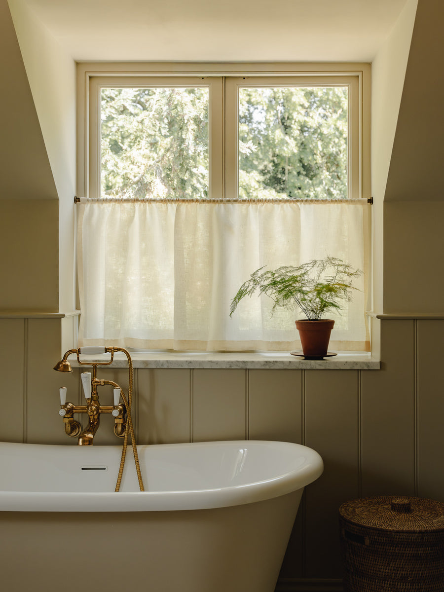 Rod pocket café curtains in cream Sera linen on a brass pole, for bathroom privacy above a roll-top bath at Baywell Studio