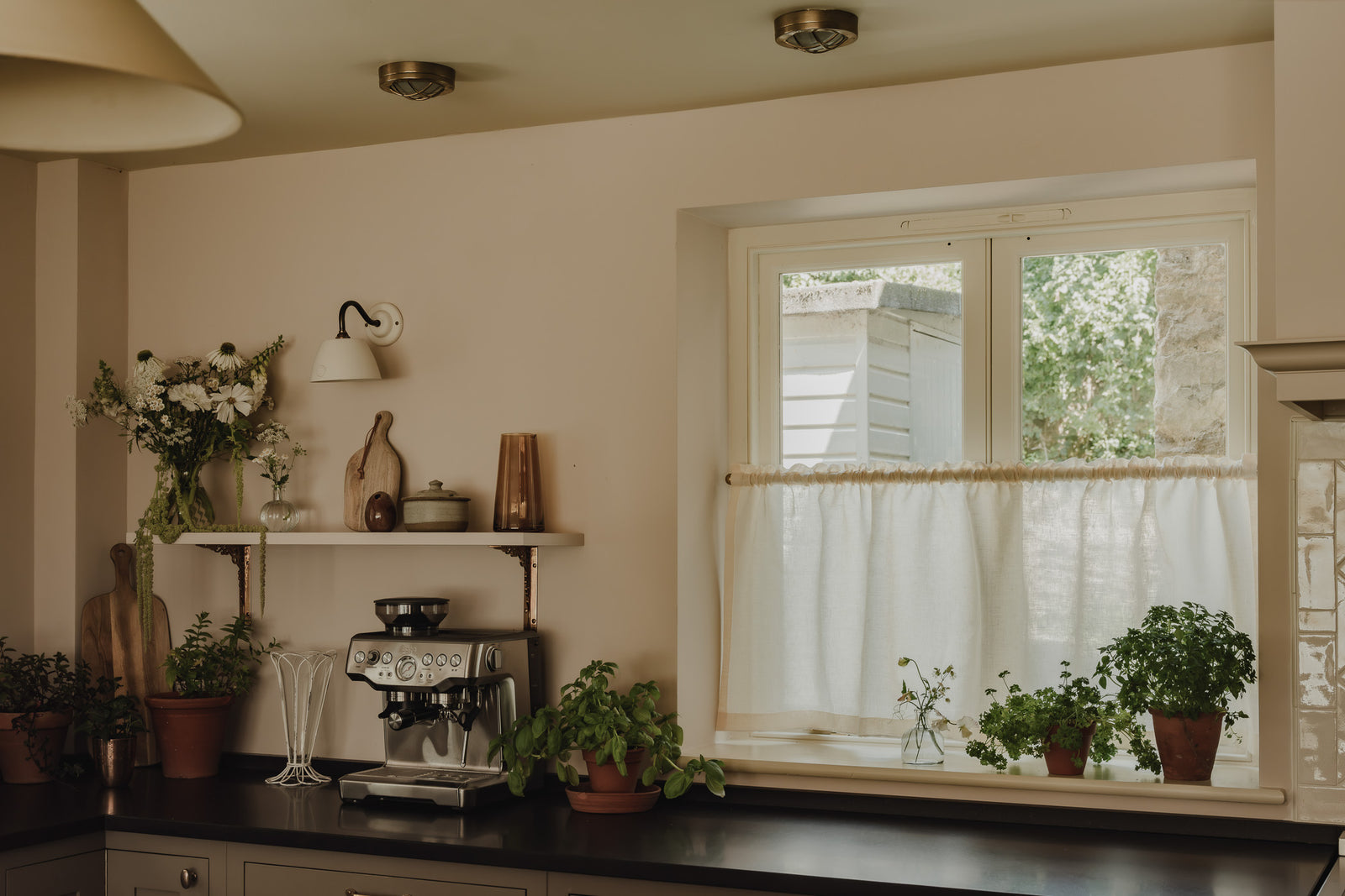 Ruffle-top rod pocket café curtain in cream Sera linen on a brass pole, in a cottage kitchen with herbs on the sill at Baywell Studio