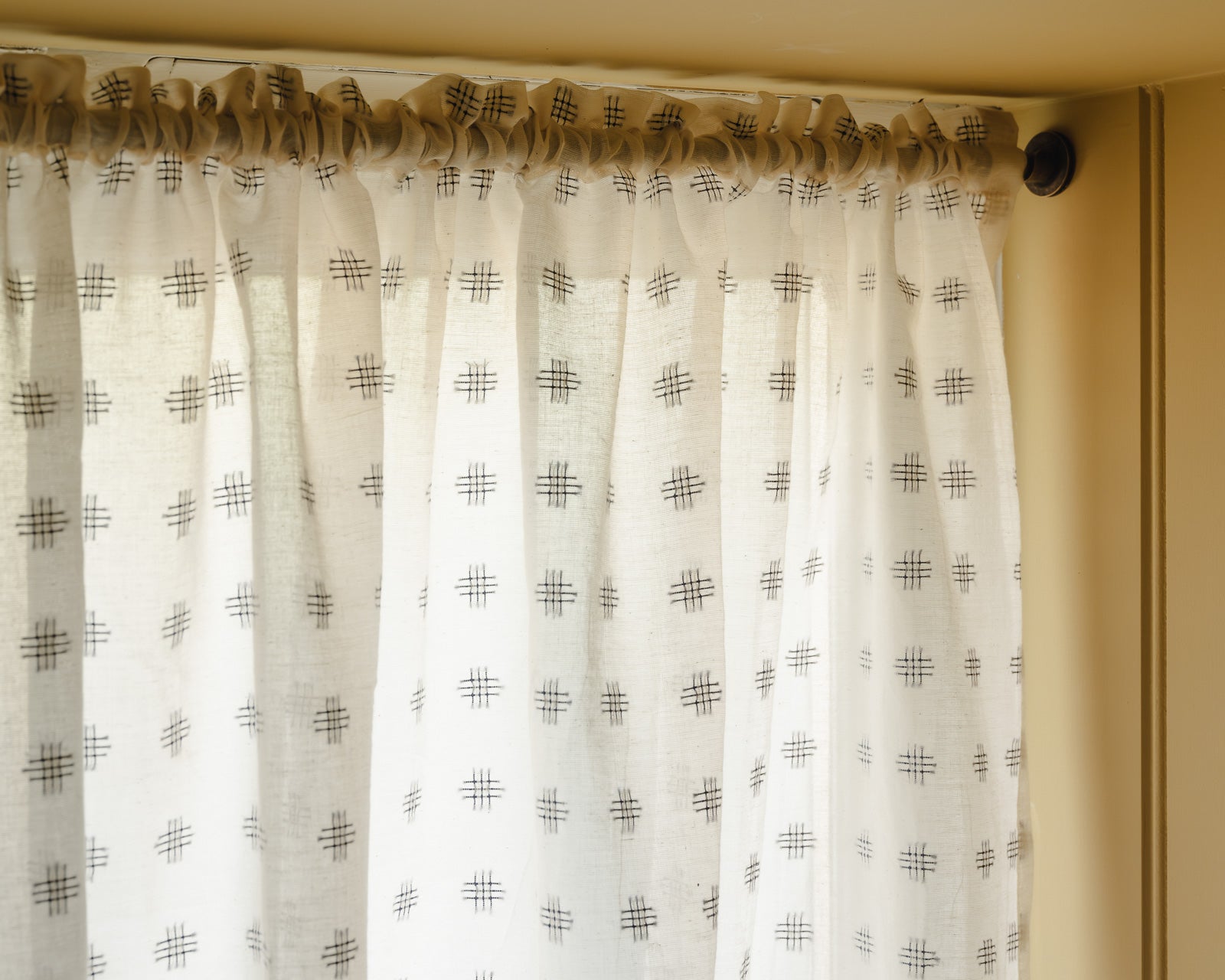 Close-up of Noma cotton in cream with a small woven indigo cross motif, a café curtain fabric at Baywell Studio