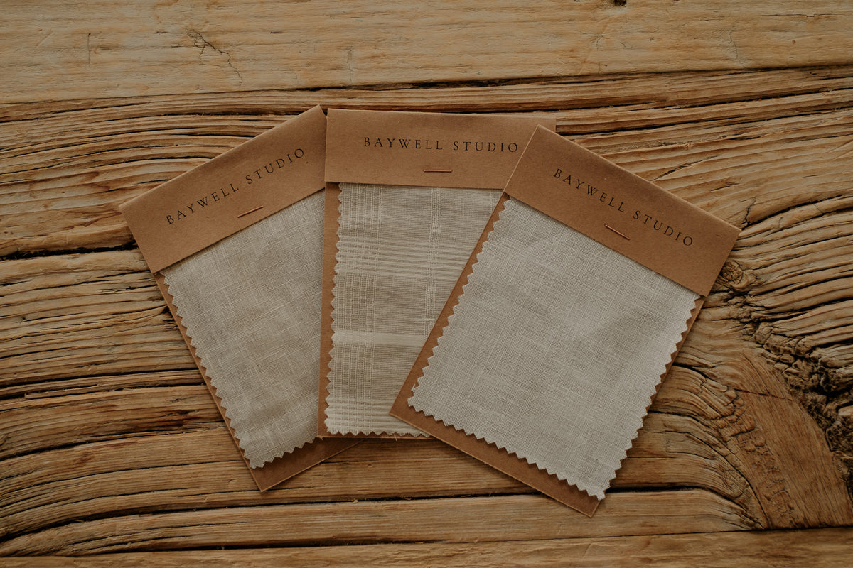 Baywell Studio café curtain fabric samples in textured cream linen and cotton, swatches on cards on rustic wood