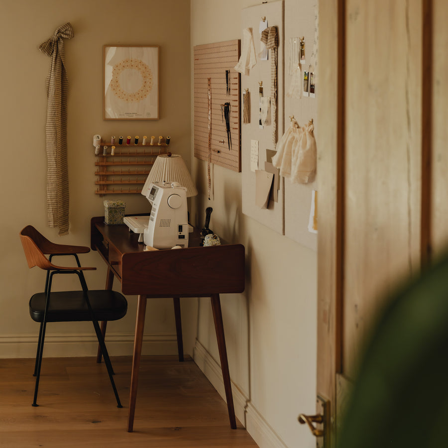 The Baywell Studio sewing corner, with a sewing machine on a walnut desk, threads on the wall, and fabric moodboards alongside