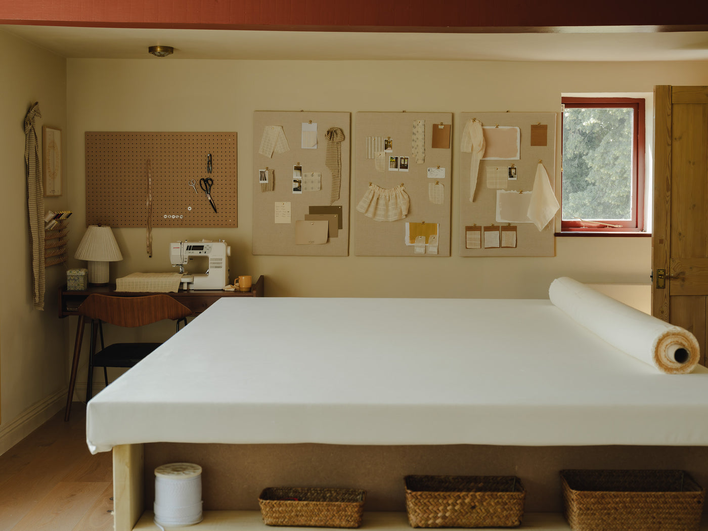 Baywell's worktable, a large cutting table with a bolt of fabric, beside the sewing desk and moodboards of fabric swatches