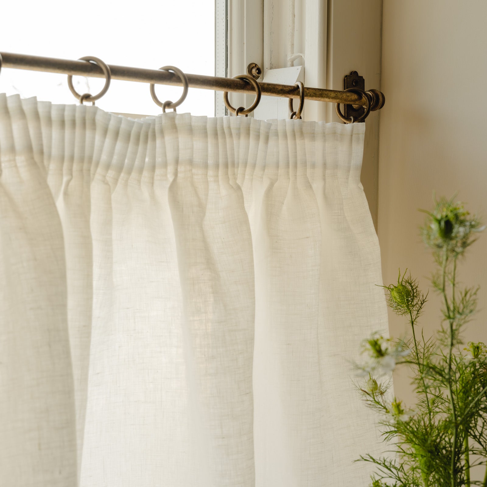Pleated café curtain in white Luma linen on a brass ring curtain pole, hanging in a hallway at Baywell Studio